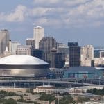 Photo of the skyline in new orleans. There are clouds over tall buildings in the background, and the superdome is in the foreground.